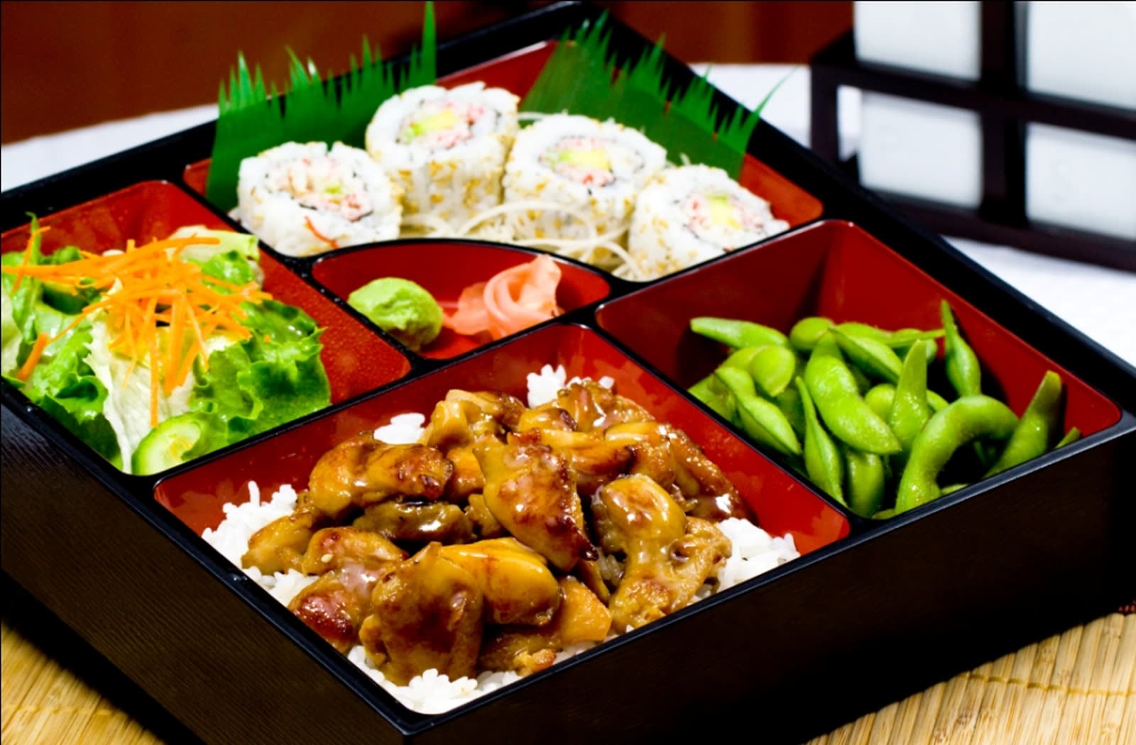 Bento box with teriyaki chicken, sushi rolls, salad and edamame